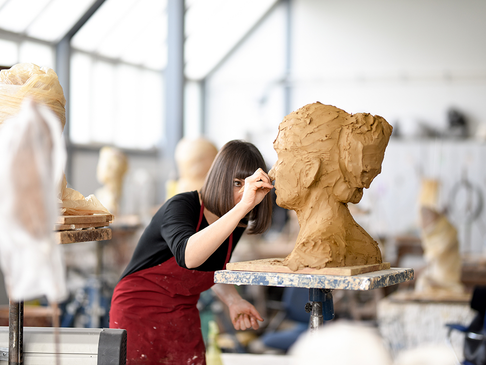 Künstlerin fertigt eine Skulptur aus Ton an.