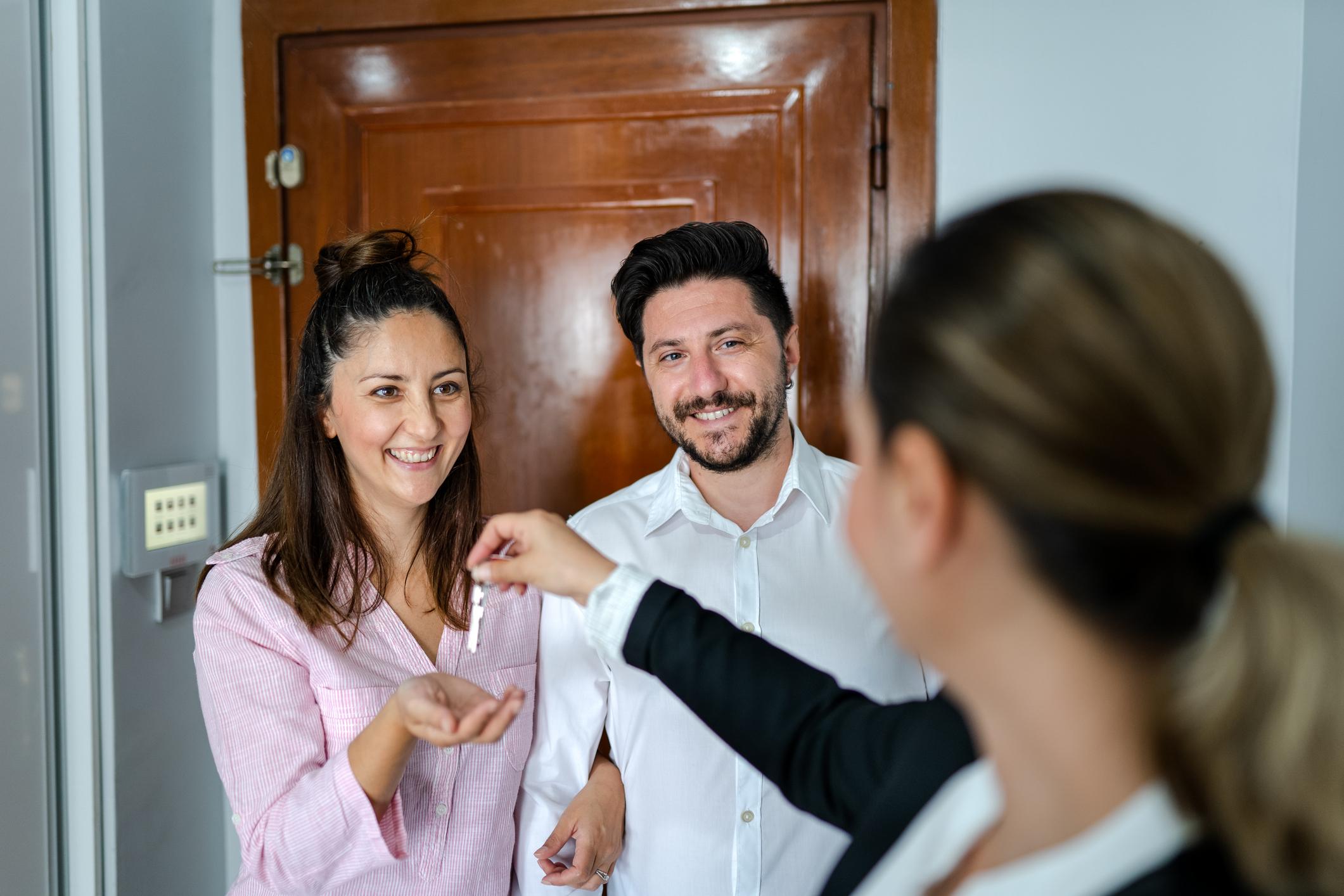Un couple reçoit les clés de son appartement de la part d'une femme.