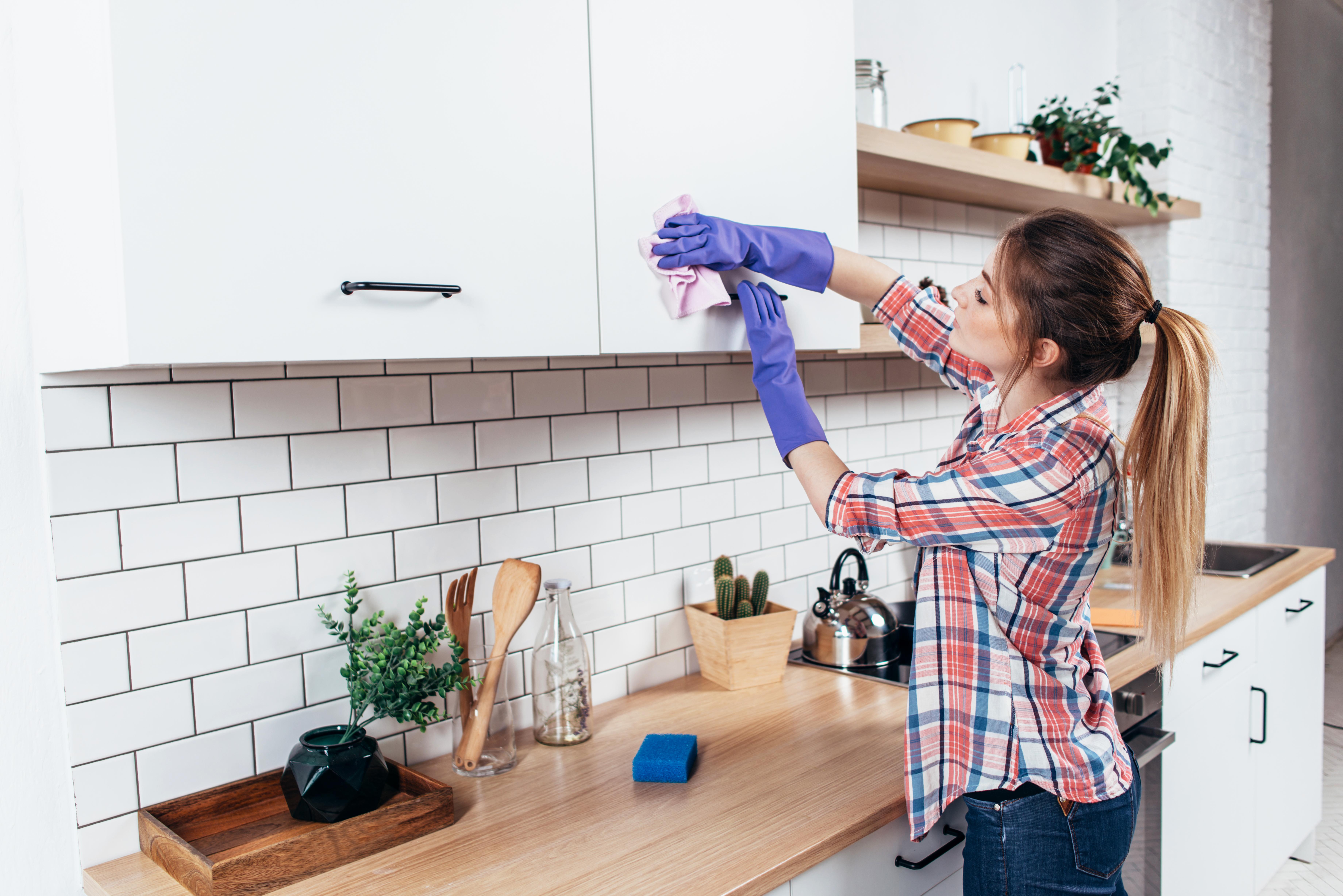 Une femme nettoie un placard de cuisine avec un chiffon humide.